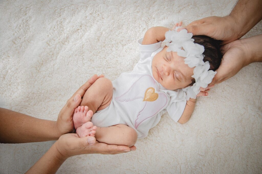 육아휴직 출산전후휴가 통합신청 을 표현하기 위한 흰 이불 위에 누운 신생아를 부모의 두 손이 감싸는 따뜻한 장면